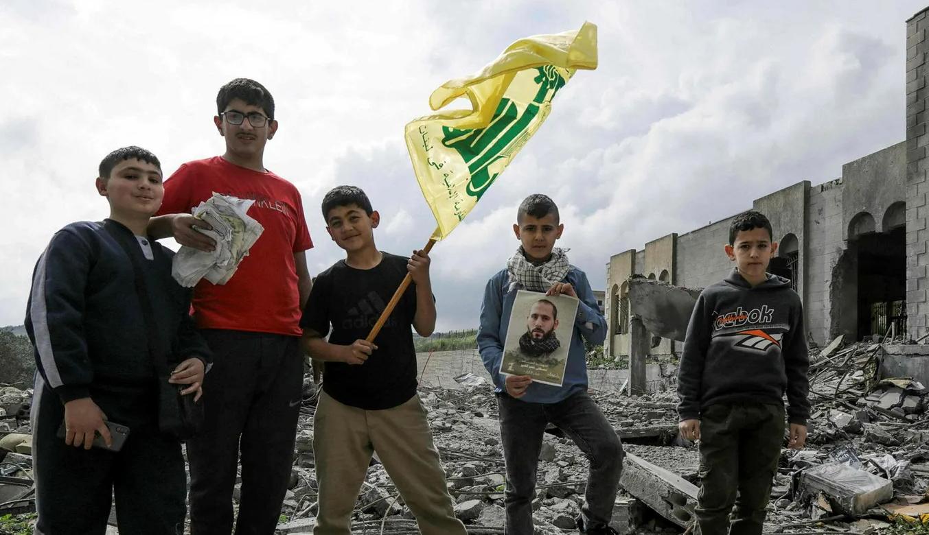 أطفال لبنانيون يحملون علم حزب الله فوق ركام منزل دمره القصف الإسرائيلي في عيتا الشعب (عن "هآرتس")
